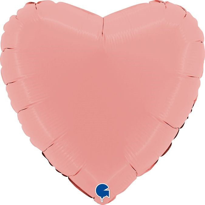 A heart-shaped foil balloon in a soft pink color, shown inflated against a plain white background. A small blue and white logo is visible at the bottom tip.