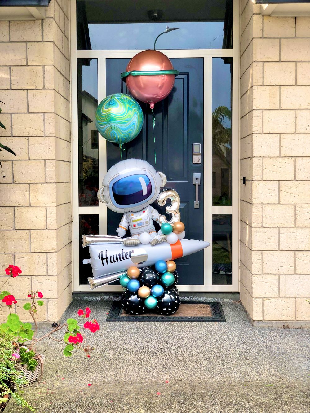 Astronaut Balloon Bouquet design with Astronaut Balloon, Air plane balloon, and orange and green Orbz balloons outside a house door
