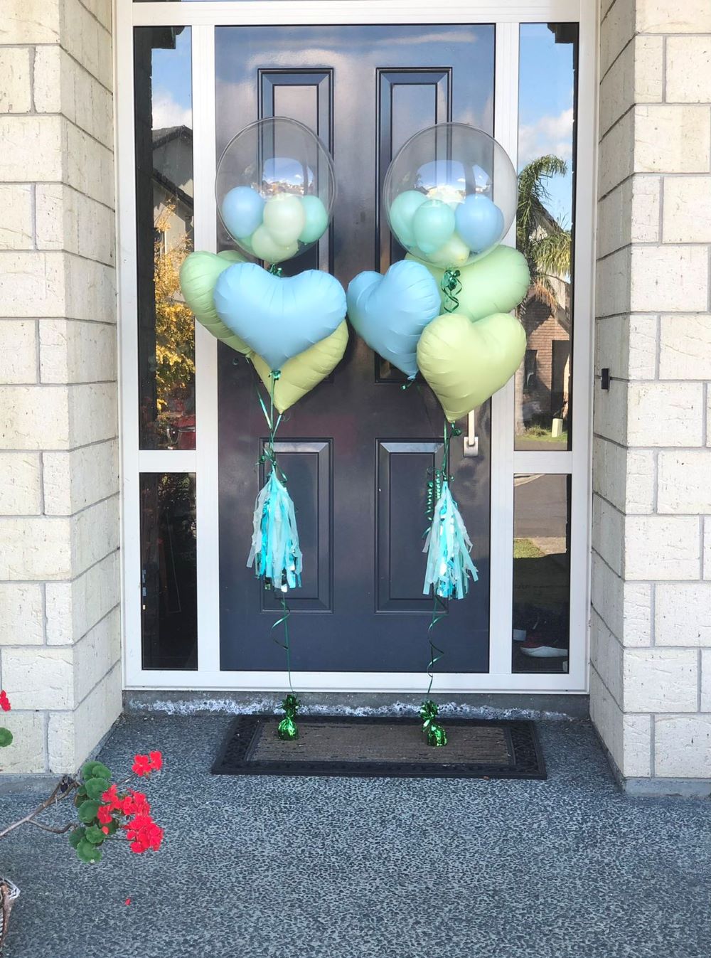 My Party Box Bubble Gum Balloon Bouquet with one bubble balloon with mini latex balloon inside and one pastel blue foil heart balloon, one Pastel green foil heart balloon and one pastel yellow  Heart Balloon in front of door