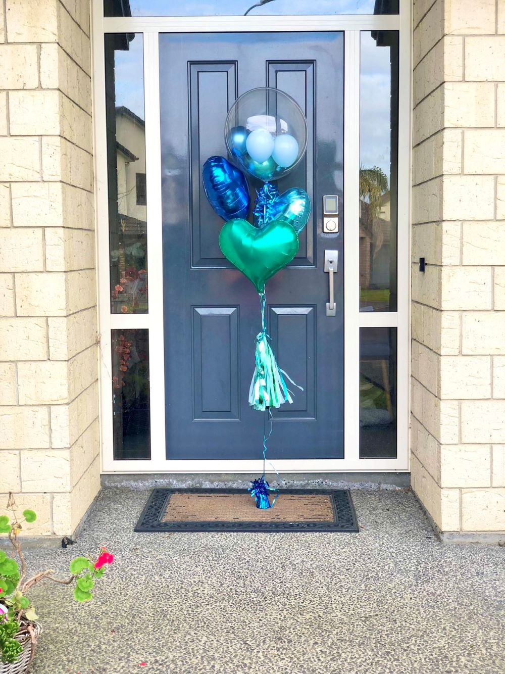 My Party Box Bubble Gum Balloon Bouquet with one bubble balloon with mini latex balloon inside and one dark blue foil heart balloon, one light blue foil heart balloon and Green Foil Heart Balloon in front of a gate