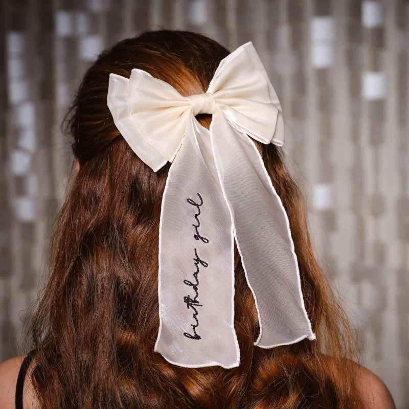 Long-haired woman wearing a white sheer organza bow with "Birthday Girl" in black script.