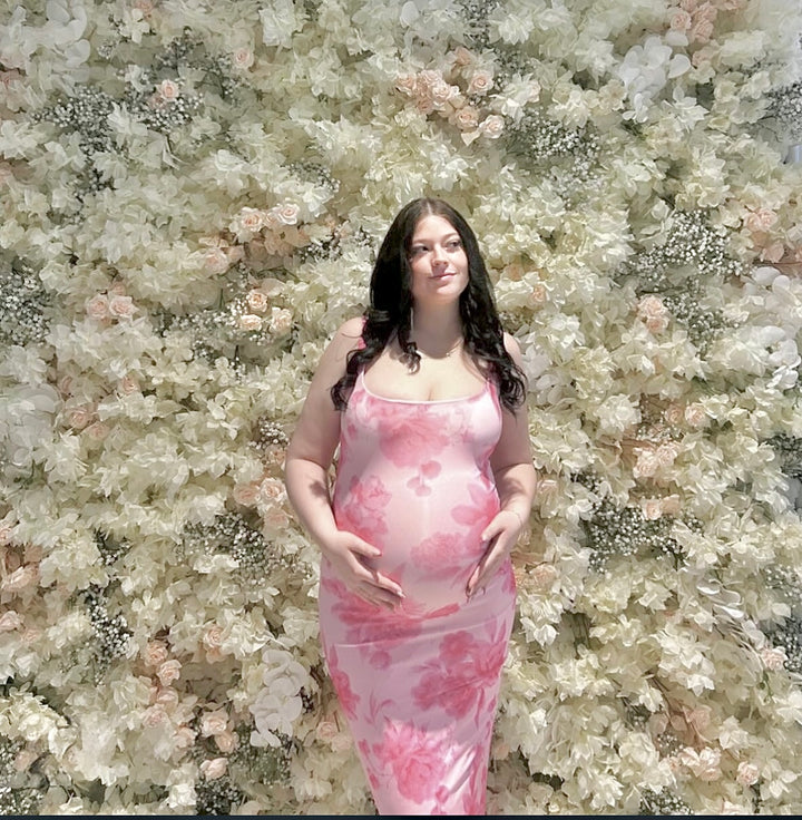 Woman in a pink floral dress standing against a floral wall