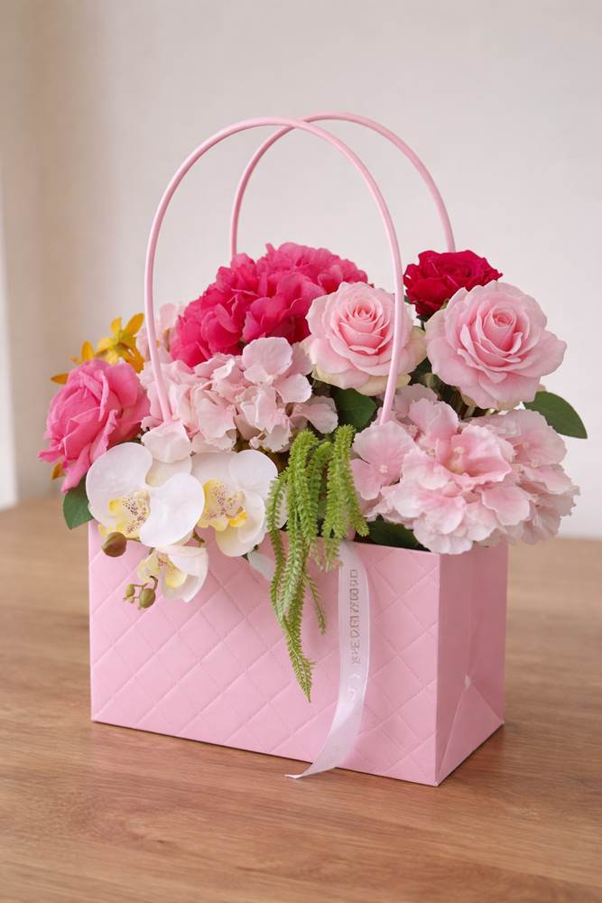 Pink floral arrangement in a decorative box on a wooden surface with a light background