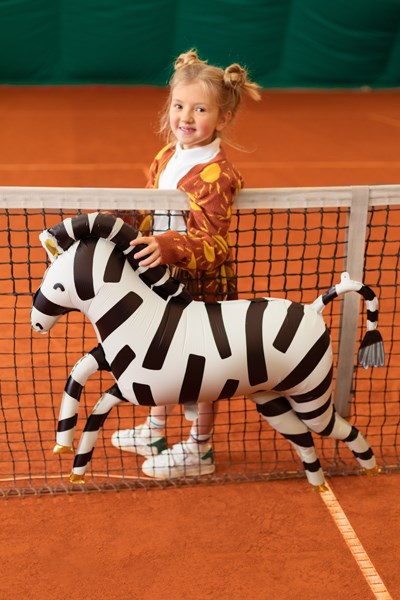 Child holding a zebra-shaped toy on an orange tennis court