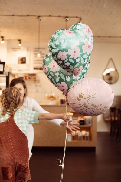 Two people in a kitchen holding floral-patterned balloons.