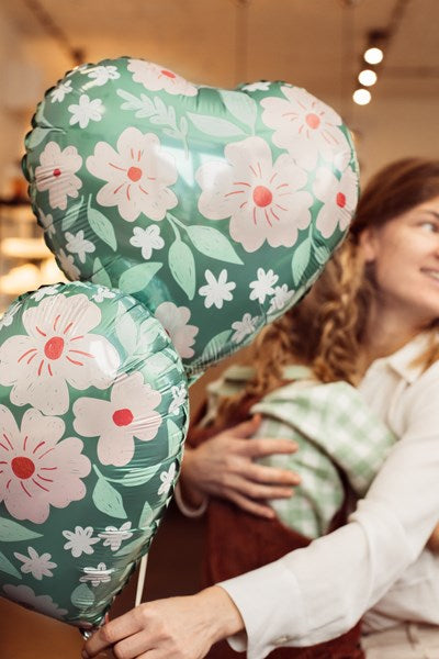 Heart-shaped balloons with floral design held by a person indoors.