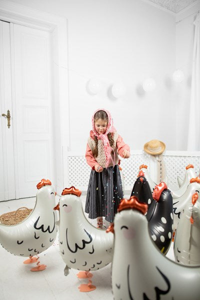 Child standing in a room with inflatable chicken decorations on a white wall.