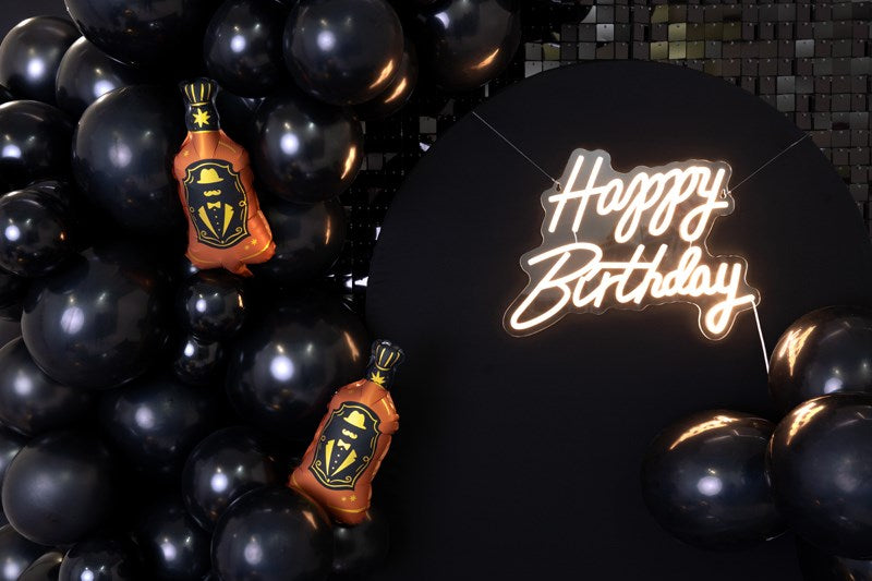 Decorative setup with black balloons, a bottle-shaped decoration, and a 'Happy Birthday' sign.
