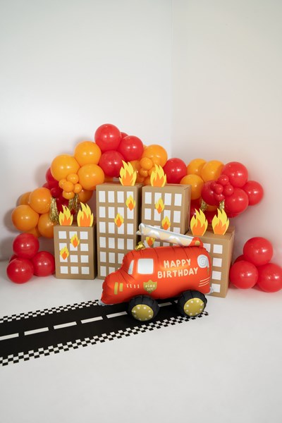 Fire truck-themed birthday setup with balloons and road on a white background