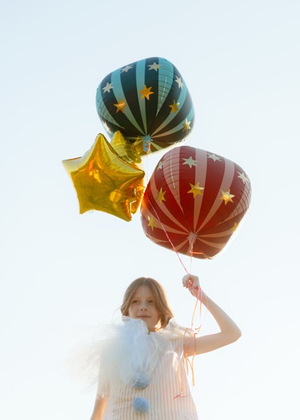 Child holding colorful balloons against a clear blue sky