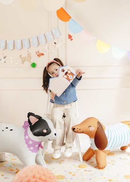 Child playing with stuffed animals in a room decorated with colorful balloons and a banner.