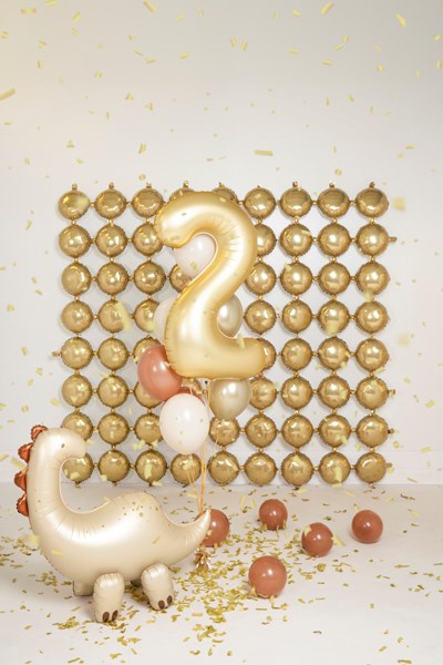 Decorative setup with gold balloons, a dinosaur figure, and number '2' against a gold ball backdrop.