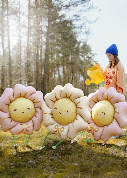 Three flower-shaped balloons with smiling faces in a forest setting.