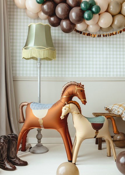 Two rocking horses in a room with balloons and a lamp.