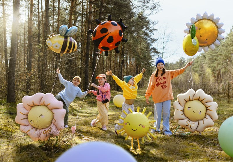 Children and adults holding colorful balloon animals in a forest setting