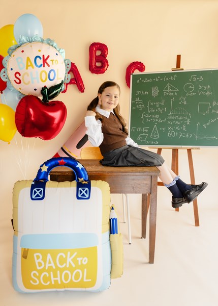 Child sitting at a desk with 'Back to School' balloons and a chalkboard in the background