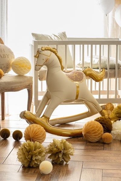 White and gold rocking horse balloon in a nursery with decorative items on the floor.
