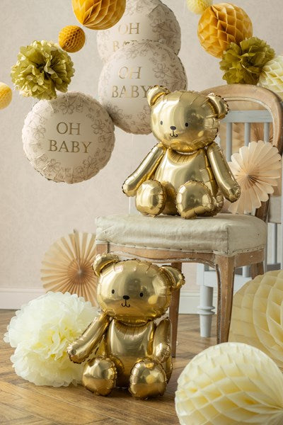 Gold teddy bears and decorative balloons on a chair with 'OH BABY' text in a neutral setting.