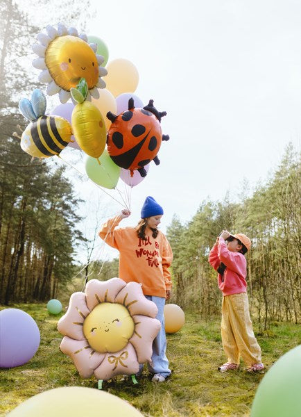 Two children holding colorful balloons shaped like flowers and animals in a forest setting.