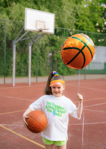 Young girl holding a basketball and a balloon shaped like a basketball on a basketball court.