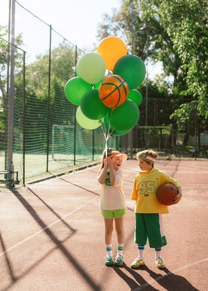 Two children on a basketball court with balloons and a basketball.