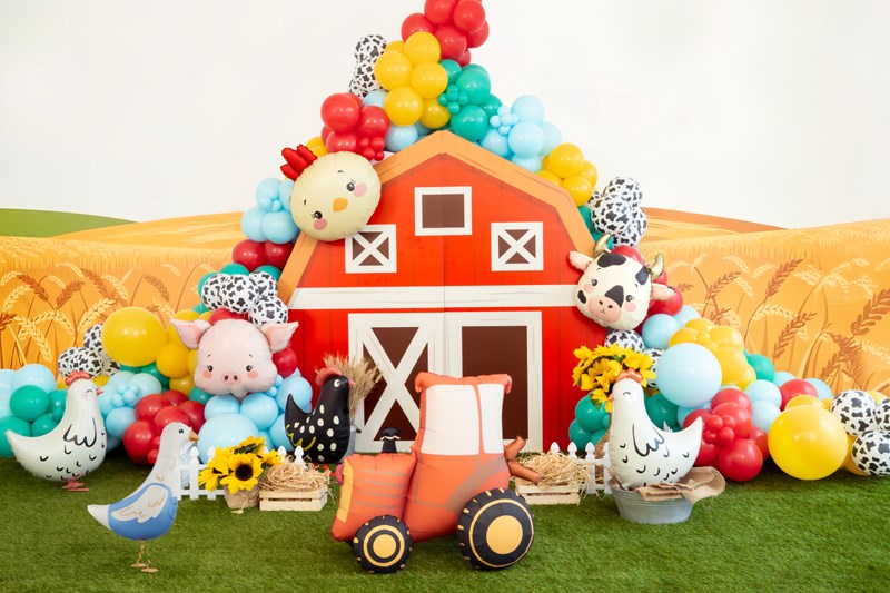 Decorative setup with a red barn, farm animals, and balloons on a grassy field.