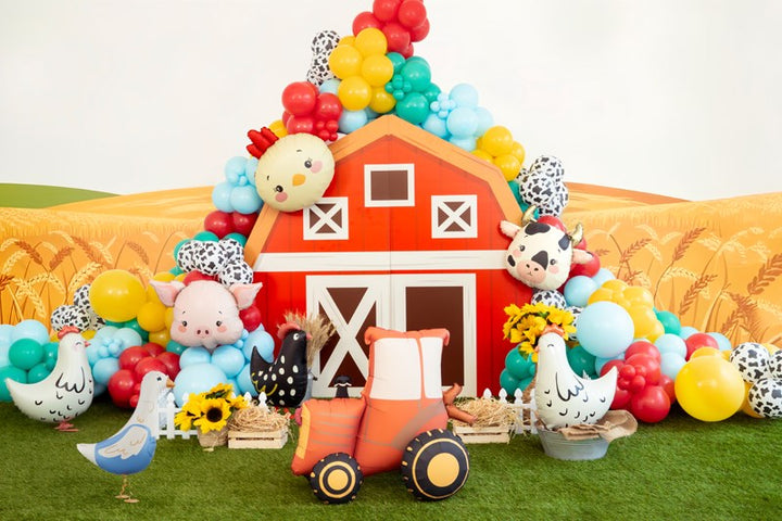 Decorative setup with a red barn, farm animals, and balloons on a grassy field.