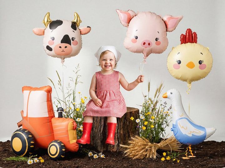 Child in a red dress and red boots holding pig-shaped balloons with farm-themed decorations.