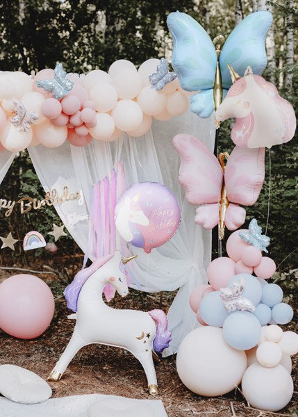 Colorful balloon arch with butterfly and unicorn decorations in a natural setting.