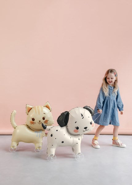 Child with inflatable cat and dog balloons against a pink background