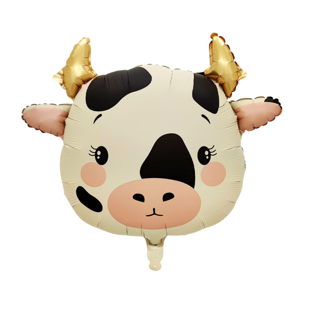 A foil balloon shaped like a cartoon cow face, with a cream-colored body, black spots, pink cheeks and snout, and shiny gold horns, shown on a plain white background.
