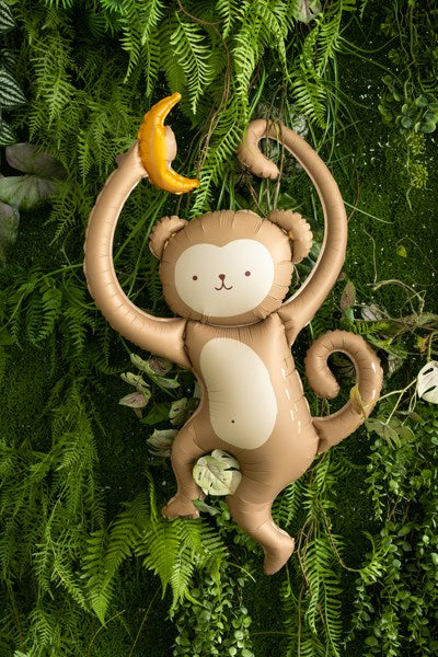 Inflatable monkey toy with a banana on a green leafy background