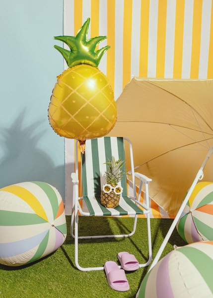 Pineapple-shaped lamp on a striped chair with beach balls and an umbrella in the background