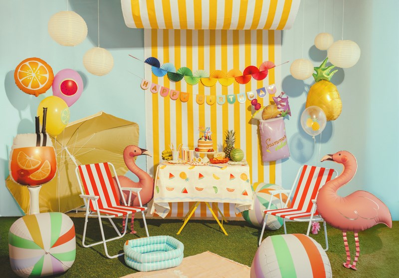 Colorful party setup with striped chairs, balloons, and a cake under a striped canopy.