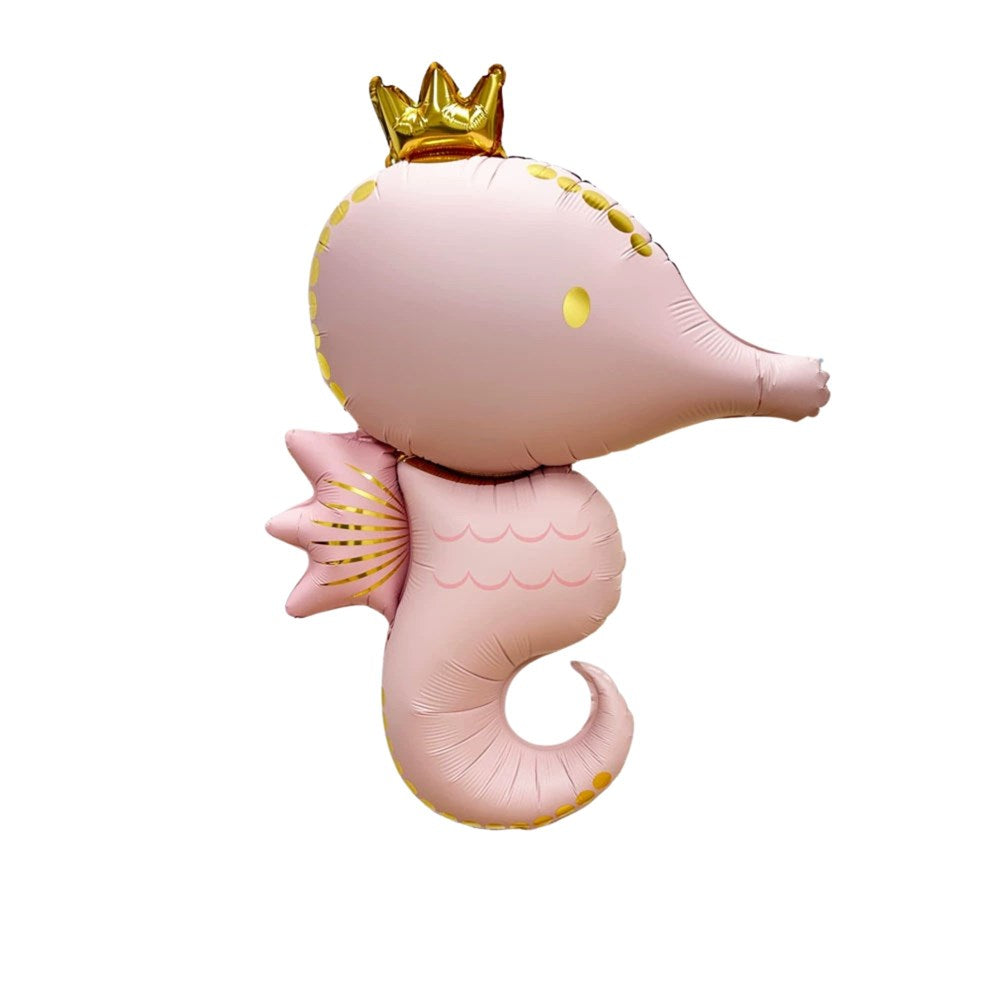 A pink foil balloon shaped like a seahorse, decorated with a small gold crown on its head, gold scalloped trim along the back and tail, and a pink fin with gold dots on the side, shown on a plain white background.
