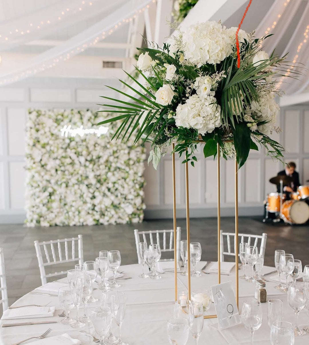 Decorative floral arrangement on a table with white chairs and a white wall in the background.