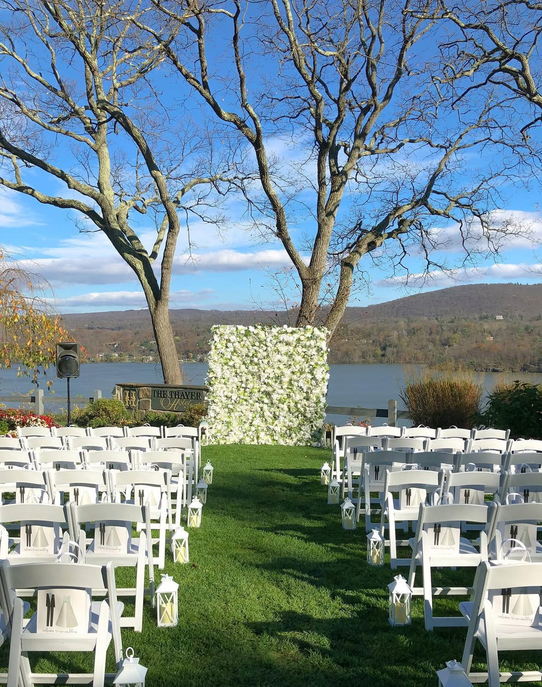 Outdoor wedding setup with white chairs and floral backdrop by a lake.