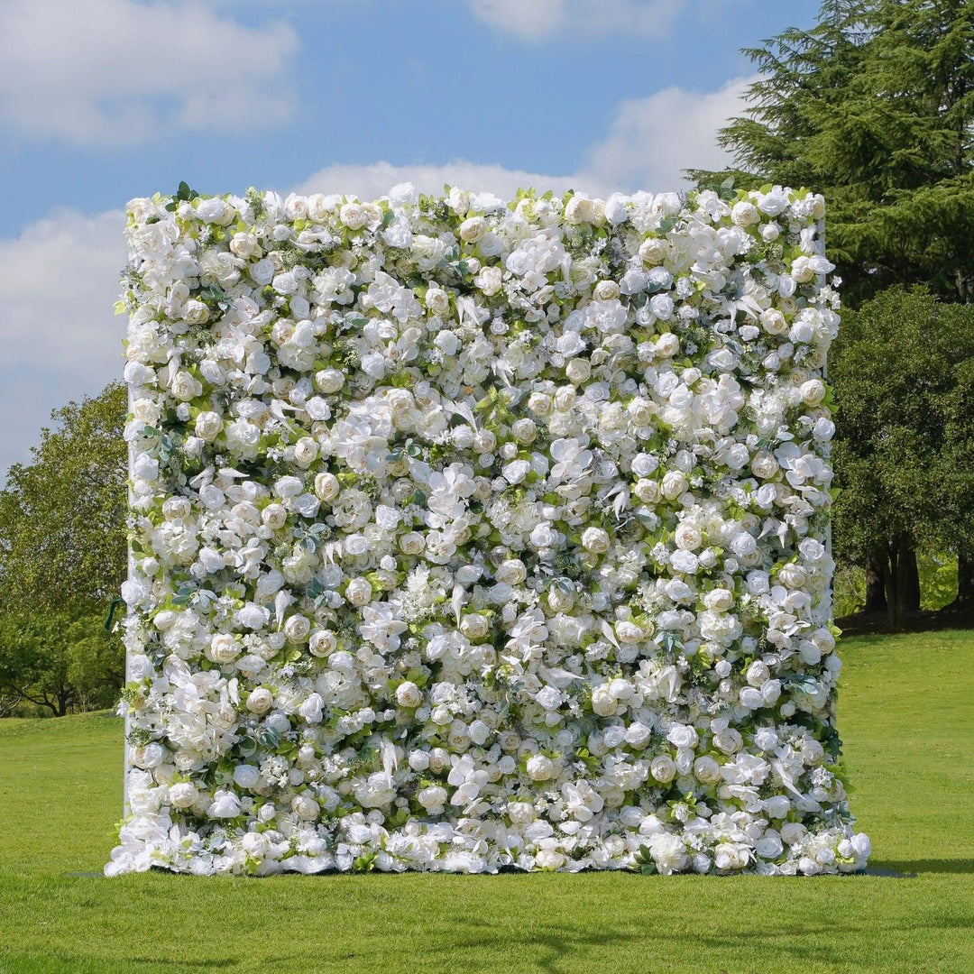 Floral wall made of white flowers on a grassy field with trees and blue sky in the background