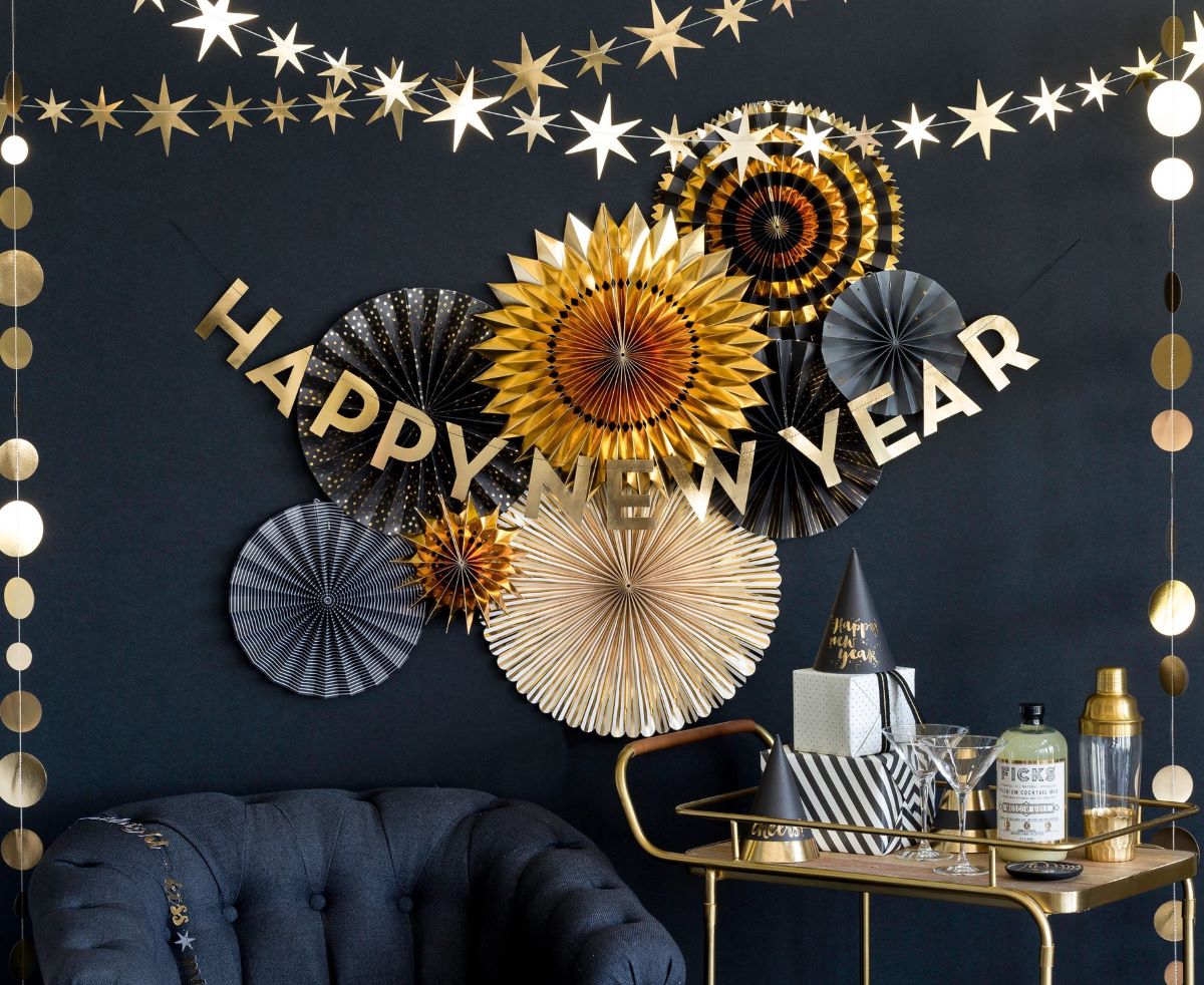 My Mind's Eye Black and Gold Party Fans Set with different shapes and colors hanging on black wall backgroupd and with Happy New Year Baner