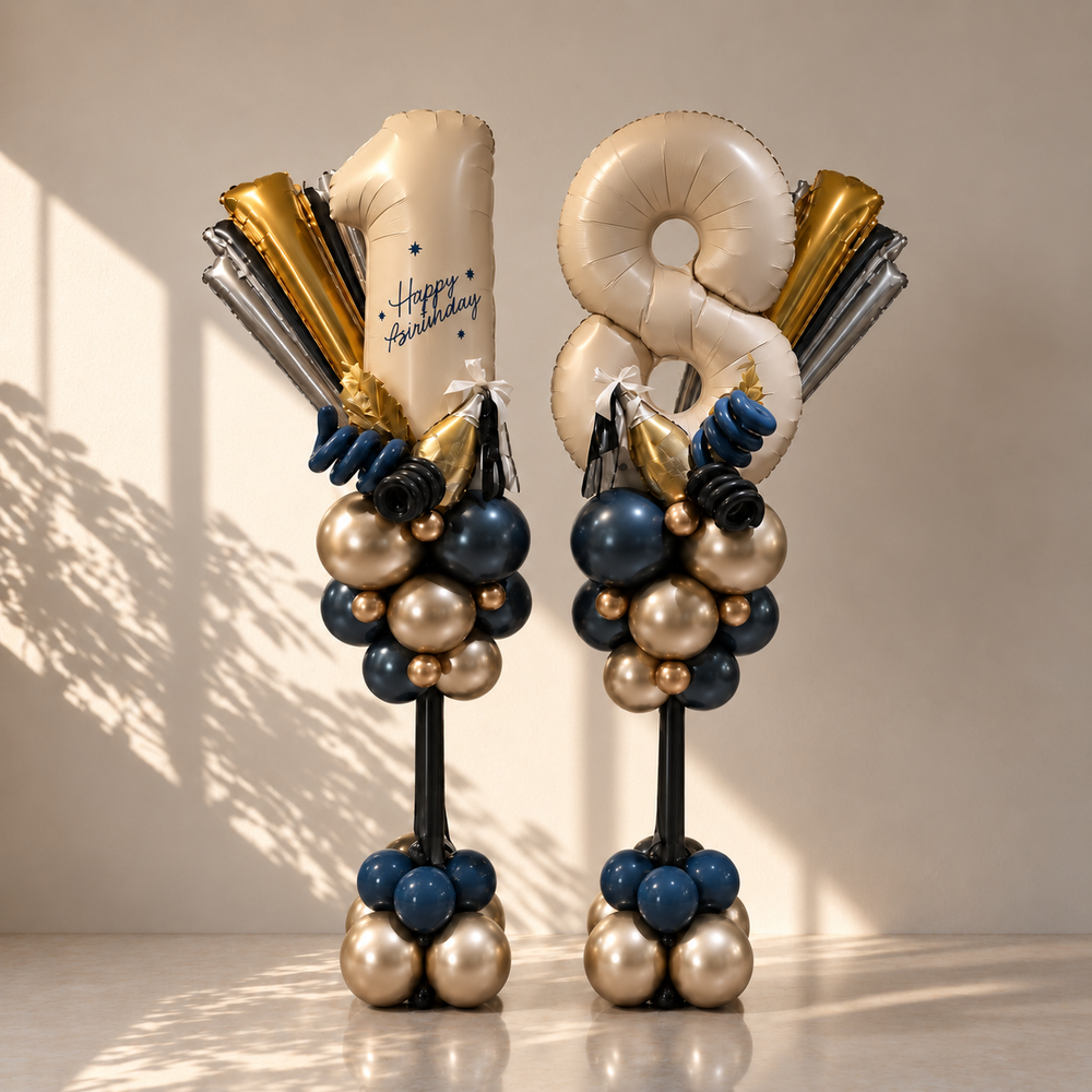 Two birthday balloon towers standing on a glossy floor against a warm beige wall. Each tower features large metallic foil balloons shaped like the numbers 8 and 1, with a 'Happy Birthday' message balloon, surrounded by clusters of navy blue, champagne gold, and silver balloons on black supports.