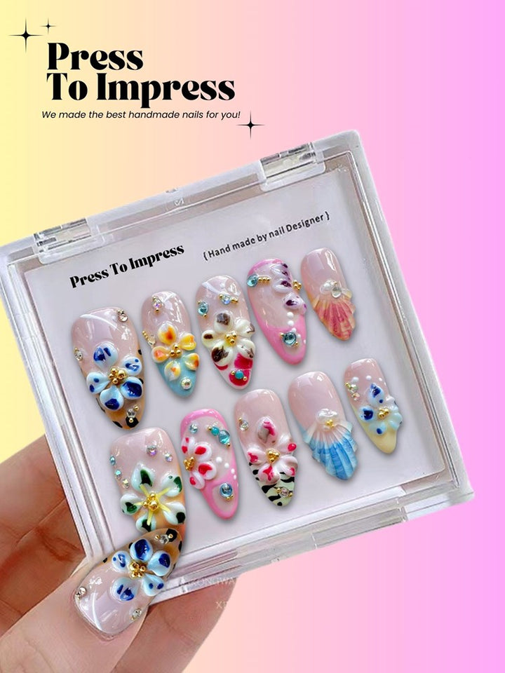 A hand holds a clear plastic case displaying ten decorative press-on nails with pastel pink bases and colorful floral and shell designs. The background is a soft pink-to-yellow gradient with the text 'Press To Impress' and 'We made the best handmade nails for you!' at the top.