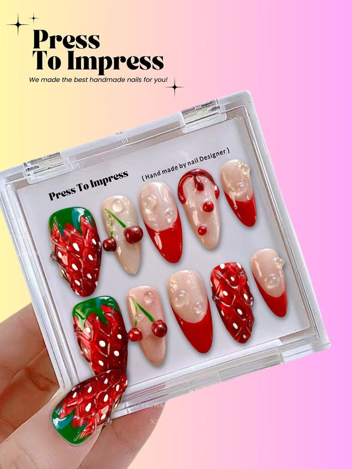 A hand holds a clear plastic case displaying 10 press-on nails with a strawberry and cherry theme, set against a pink and yellow gradient background with 'Press To Impress' branding.