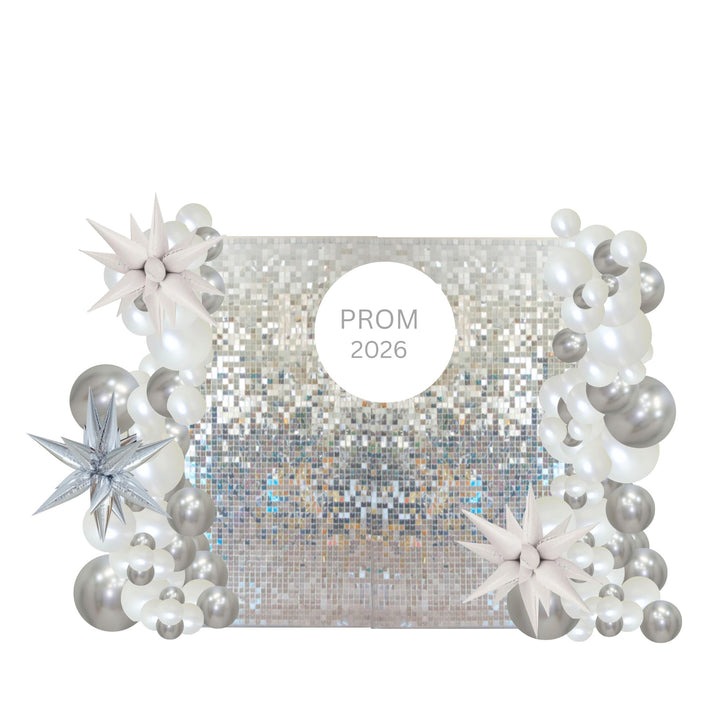 A square silver sequin backdrop decorated with white and silver balloon garlands, star-shaped balloons, and a central white circle reading 'PROM 2026'.