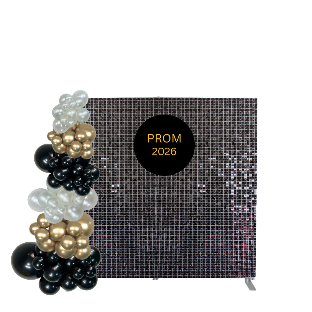 A black sequin prom backdrop with a black circular sign reading 'PROM 2026' in gold, styled with a balloon arch in black, white, and gold balloons on the left, against a plain white background.