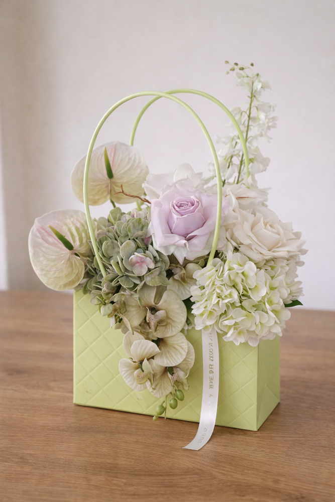 Pastel floral arrangement in a light green basket on a wooden table.