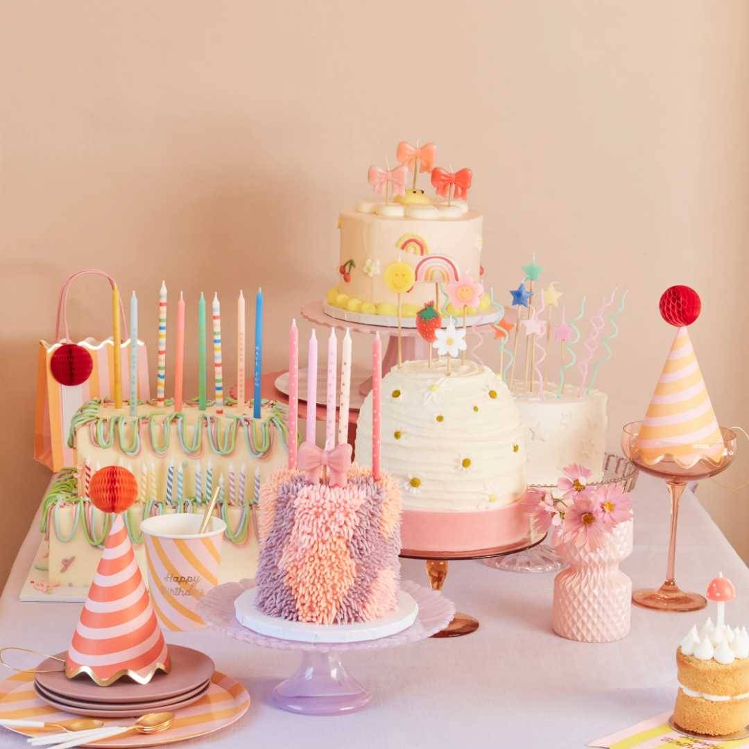 Pastel birthday cakes and party hats on a decorated dessert table.
