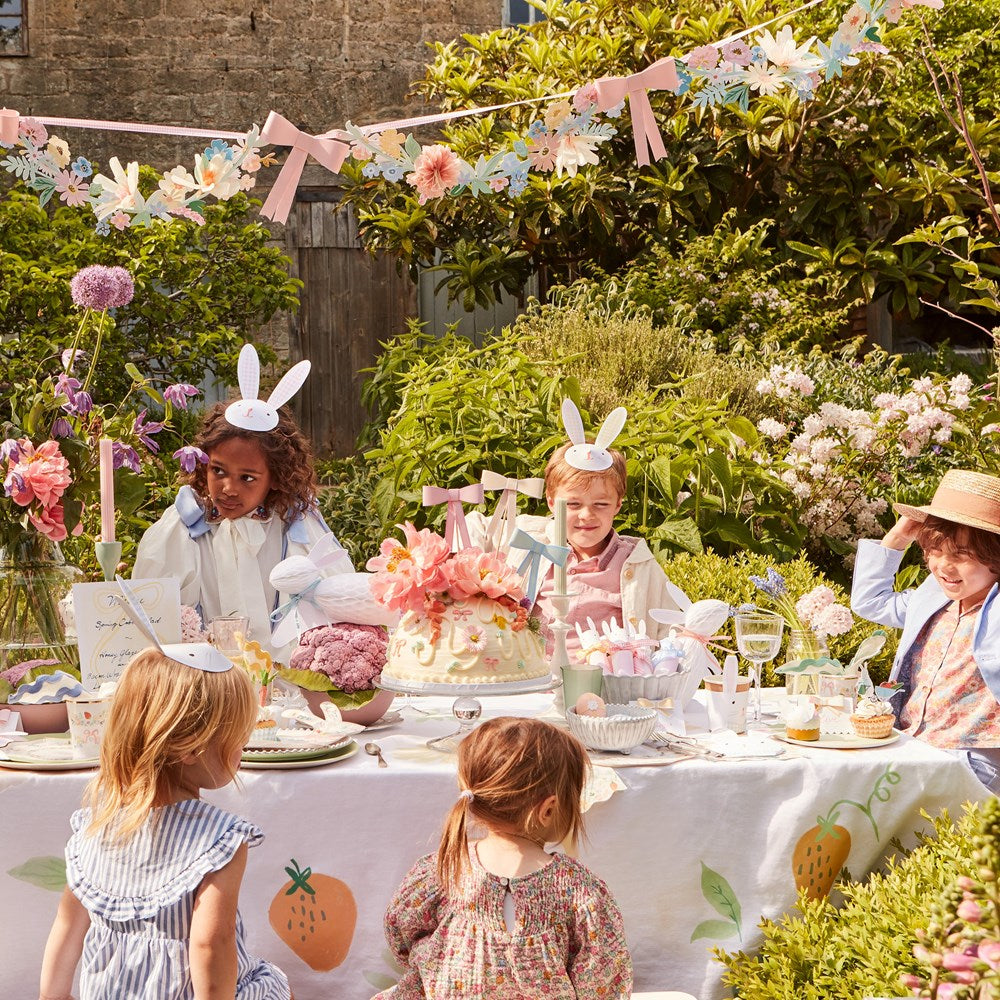 Children at a garden party with floral decorations and a table set for a celebration.