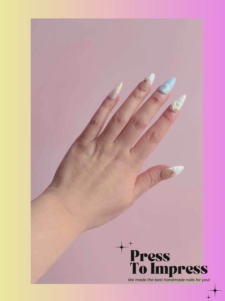 A video shows A hand holds a clear plastic case displaying ten decorative press-on nails with pastel designs including beige, light blue, white, and yellow star details. The background is a pink-to-yellow gradient with the text 'Press To Impress' and 'We made the best handmade nails for you!' in the top left.