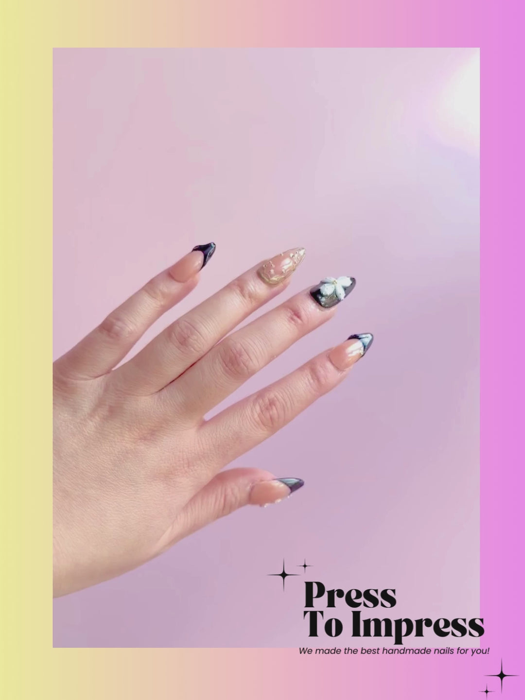 A Video shows A hand holds a clear plastic case displaying press-on nails. The nails are almond-shaped, featuring a mix of nude beige, glossy black, and white floral designs with gold glitter accents.