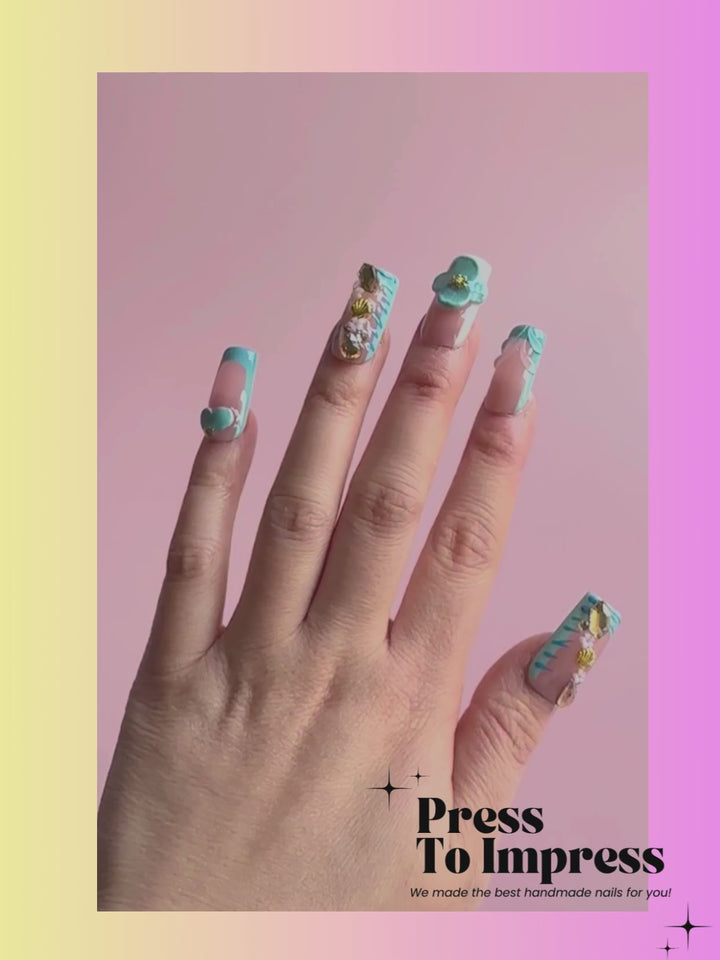 Video shows A hand holds a clear plastic case displaying 10 decorative press-on nails. The nails feature a peach nude base with blue stripes, blue flowers, gold glitter, and white floral details.